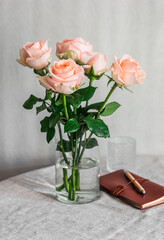 A bouquet of delicate roses in a glass vase and a leather notebook on a table in a bright room