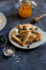 Crepes with honey, mint leaves, blueberries on gray stone background. close up with copyspace. Delicious crepes, thin pancakes