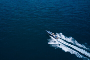 Boat performance drone view. Performance speedboat moving fast on blue water aerial view. Dark gray blue boat in motion at sea.