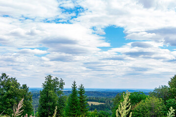 Natural beautiful landscape. View from mountain on forest valleys against blue cloudy sky. National park, layered Hills. Lookout point. Deciduous and coniferous forest,