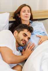 Delighted father tenderly lie down on belly of beloved pregnant wife on bed to feel and hear unborn baby kicking in stomach