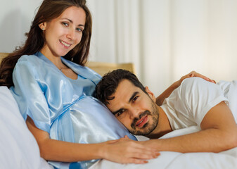 Obraz premium Pregnant wife resting on bed at night and smile as happy that beloved husband care her maternity by tenderly lying down on belly of unborn baby to listen child kicking