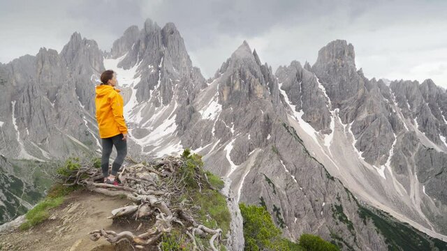 4K  Majestic rocky mountain peaks with woman in foreground wearing yellow jacket and enjoying landscape. Travelling, hiking, backpacking, exploring nature concept. Dolomite Alps, South Tyrol, Italy
