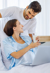 Lovely pregnant wife tenderly touch beloved belly of unborn baby while lounging on bed with smile and happy as enjoy watching entertainment media on computer