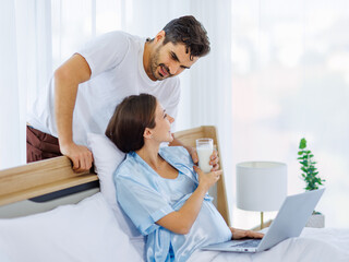 Lovely pregnant wife tenderly touch beloved belly of unborn baby while lounging on bed with smile and happy as enjoy watching entertainment media on computer