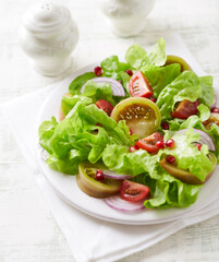 Salad with red and green Tomatoes and Pomegranate Seeds on bright wooden Background. Close up.