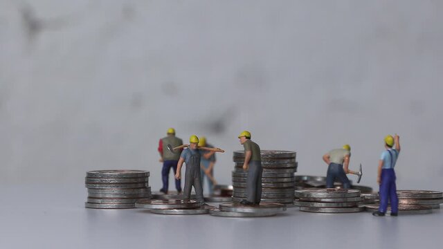 Wage and labor concept. Miniature workers working with piles of coins.
