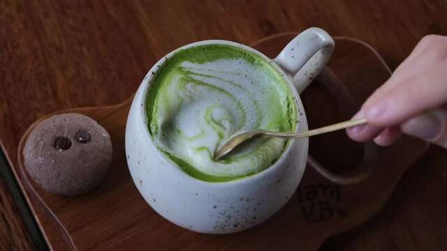 Human hand mixing foam on trendy vegan matcha latte with a spoon, detox hot drinks in a hipster cafe