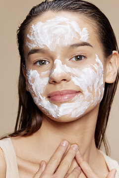 Smiling young woman skin care by using white mask on the face beige background
