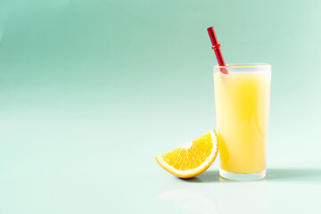 Natural orange juice in a transparent glass with a slice of orange and a bright red tube on a green background place for text
