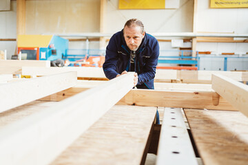 Factory foreman checking a large wooden beam for warp