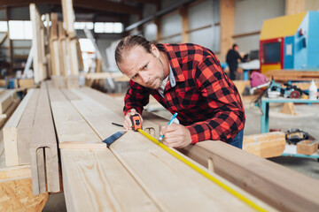 Man working in industrial woodworking factory taking measurement