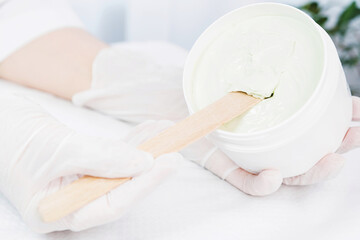 Close up photo of cosmetologist hands in medical gloves holding a jar of cream product scrab and tries to take it out of the jar in cosmetologist cabinet.