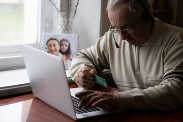 Senior man using laptop and headphones online.