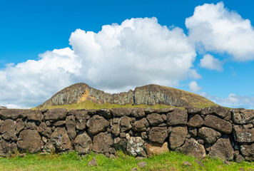 Wall in volcanic rock with the Rano Raraku mountain and quarry with stones for Moai statue...
