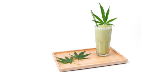 A glass of cannabis smoothie with cannabis leaves in a wooden tray on a wooden table isolated over white background. Copy space backdrop artwork design banner. Eatable vegetable healthy concept ideas