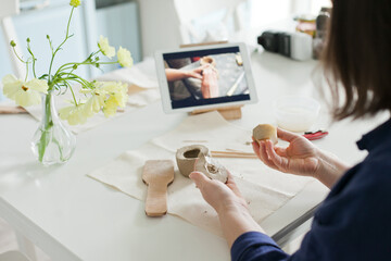 woman watching an online masterclassl and sculpting a small pumpkin out of clay with tools - DIY...