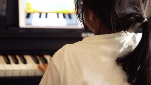 Asian woman is practicing  piano with online Music lesson on tablet, Back view.