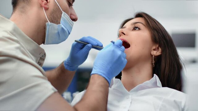 Closeup male dentist examining teeth at female patient open mouth use mirror and stomatology tools
