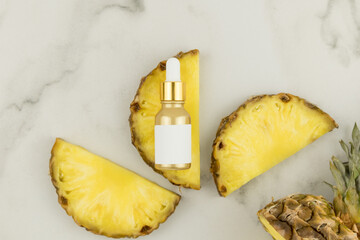 a gold matte bottle with cosmetic whey or pineapple oil lies on a slice of fresh fruit. top view. marble background. Unbranded moskap.