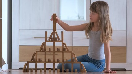 Happy child girl playing game stacking wooden toy blocks in high pile structure. Hand movement control and building computational skills concept