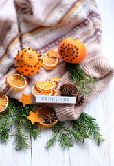 calendar block February, knitted sweater, citrus, dry orange slices, fir branches and cones on wooden rustic background. February month calendar concept. winter season