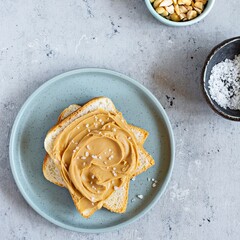 Toast (sandwich) of a slice of toast bread and peanut butter for breakfast on a blue (grey) background.