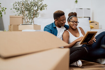A married couple after moving to a new house unpack boxes while sitting on the floor, a woman shows...