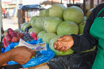 Cash, Naira notes or money exchanging hands at a fruit stand in a Nigerian local market