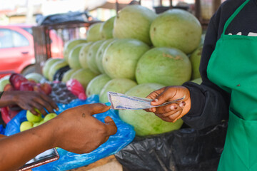 Cash, Naira notes or money exchanging hands at a fruit stand in a Nigerian local market