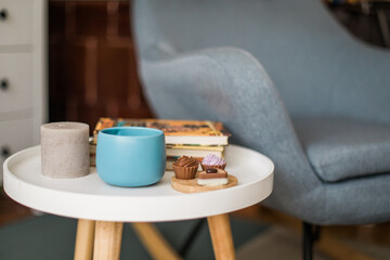 Blue cup of tea, chocolate pralines and books on a small table, armchair in background, copy space