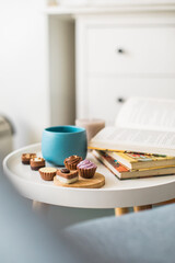 Vertical photo of book, cup of green tea and chocolate pralines on round white side table, Scandinavian design, copy space