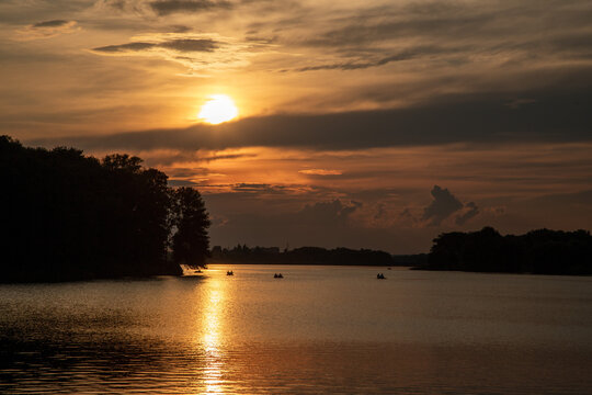 Epic Red Clouds above the lake at Sunset. People sailing on boats in City Park