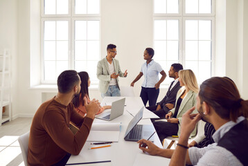 Diverse speaker lead head meeting with employees present new company project or strategy at meeting. Ethnic team leaders talk brainstorm at briefing with workers in office. Cooperation, teamwork.