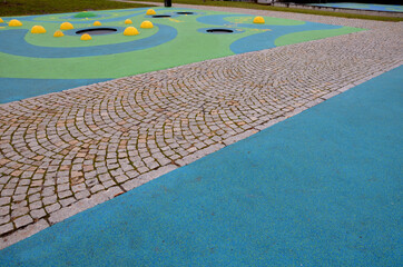 blue rubber surface of a playground with yellow scoops and colored spots in the frost of human footprints. raised lenses such as balls, wooden benches and circular trampolines sunk into the terrain.