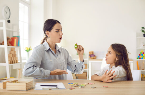 Girl Of Primary School Age Practices Correct Pronunciation With Female Speech Therapist. Child Learns Alphabet And Performs Exercises To Correct Language Deficiencies. Children Speech Therapy Concept.