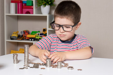 A child in glasses, a young businessman plays with coins and saves money.