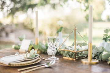 Luxury wedding reception dinning table setup with eucalyptus branches and gold geometric decoration on a rustic wooden table