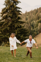 Naklejka na ściany i meble Outdoor shot of young couple in love walking on through grass field in the mountain area