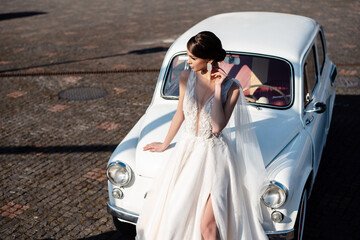 Woman in wedding dress posing near retro car outdoors