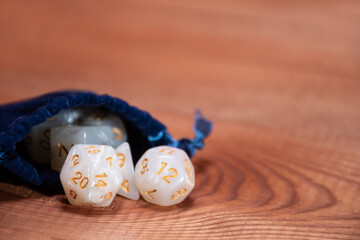 Soft focus on set of role playing white dices in blue  storage bag on a gaming table made of wood: background for role-playing games with place for text, side view