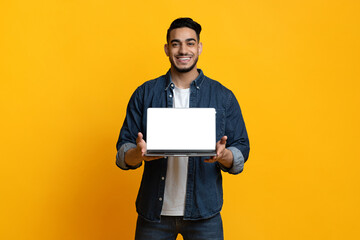 Cheerful arab guy showing laptop with blank screen