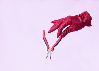 Woman's red glove holding a work tool on pink background