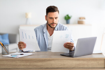 Millennial male self-entrepreneur working with papers at home office, checking annual financial reports, free space