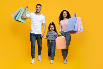 Happy Cheerful Arab Parents And Their Daughter Walking With Bright Shopping Bags