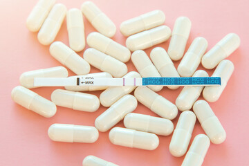 positive pregnancy test and white vitamins pills on pink background close up, pregnancy concept
