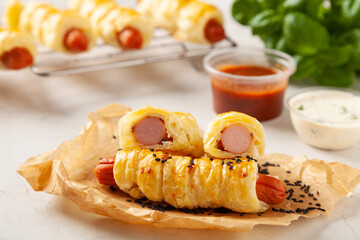 Sausage baked in puff pastry. Sprinkled with sesame seeds, served with sauce.
