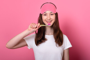 Cheerful happy caucasian brunette teen girl with freckles in sleep mask holds a toothbrush in hand...