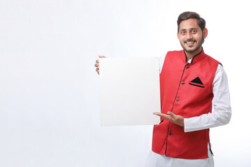 Indian man holding white board, promoting offers on festival season while wearing traditional cloths, standing over white background.