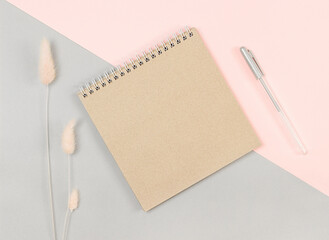 brown notebook and pen on a gray-pink background. View from above